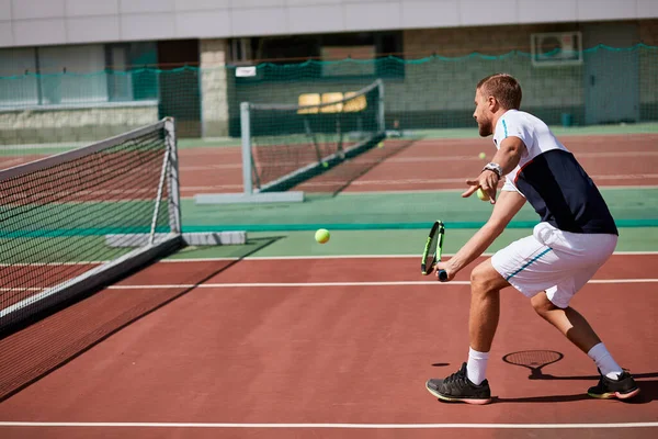Joven en ropa deportiva está jugando al tenis en la pista de al aire libre. —  Fotos de Stock