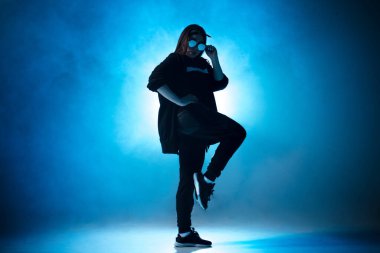Genç hip-hop kadın dansçısı mavi neon ışıklarla sahnede solo performans sergiliyor.
