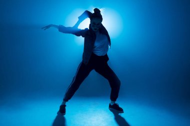 Genç hip-hop kadın dansçısı mavi neon ışıklarla sahnede solo performans sergiliyor.