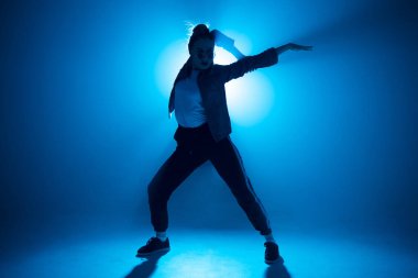 Genç bayan hip-hop dansçısı. Stüdyonun mavi ışık arka planında. İşaret fişeği efektiyle.
