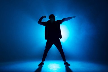 Profesyonel erkek dansçı gece kulübünde duman ve mavi neon ışıklarıyla dans ediyor.