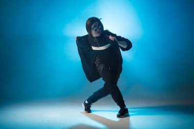 Genç hip-hop kadın dansçısı mavi neon ışıklarla sahnede solo performans sergiliyor.