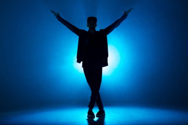 Profesyonel erkek dansçı gece kulübünde duman ve mavi neon ışıklarıyla dans ediyor.