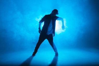 İzole edilmiş neon mavi arka planda hip hop dansı yapan genç bir dansçı.