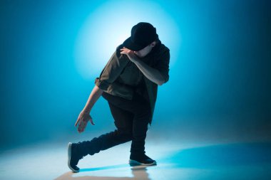 İzole edilmiş neon mavi arka planda hip hop dansı yapan genç bir dansçı.