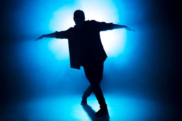 Sporty modern style hip-hop dancer shows his dance on blue studio background. — Stock Photo, Image