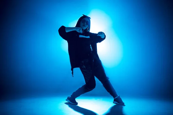 Mujer joven bailarina de hip-hop en el estudio fondo de luz azul con efectos de bengala —  Fotos de Stock