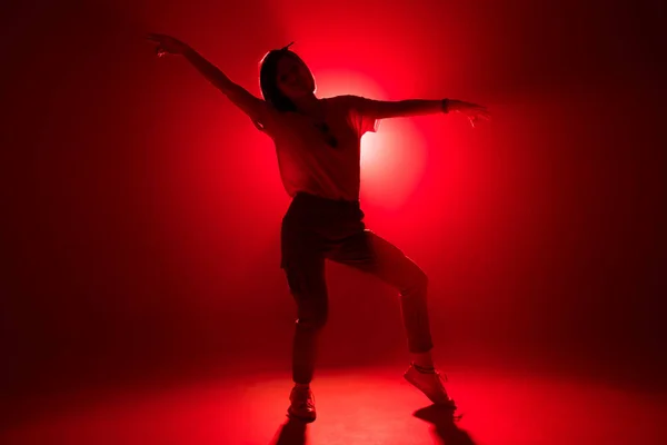 Snygg kvinnlig dansare stående i dansposerar på röd studio bakgrund — Stockfoto