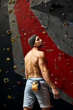 Duvarın yanında duran, kaya tırmanışına hazır bir sporcunun arkası..