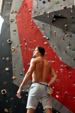 Duvarın yanında duran, kaya tırmanışına hazır bir sporcunun arkası..