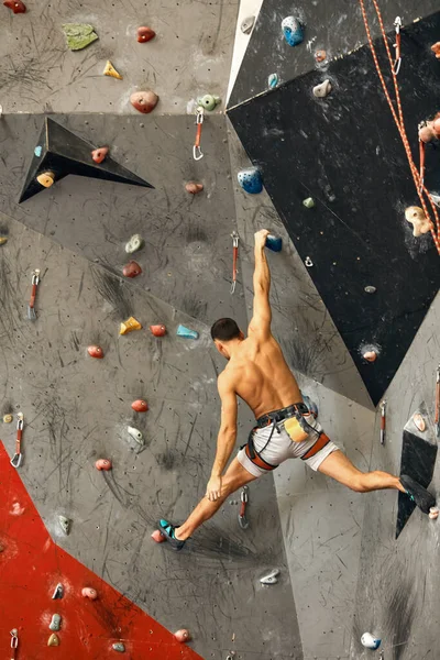 Männlicher Kletterer trainiert in Turnhalle, klettert an künstlicher Wand mit Felsbrocken hoch. — Stockfoto