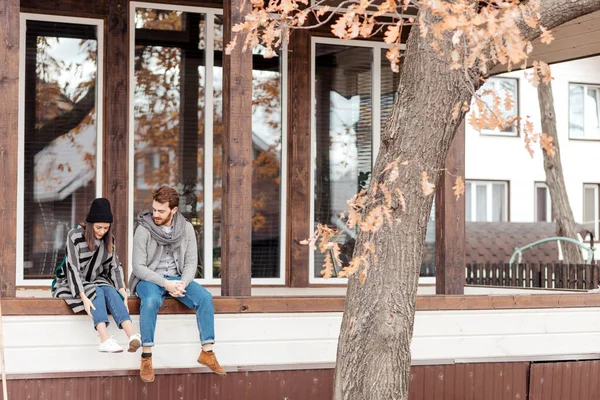 Feliz jovem casal sentado ao ar livre, na frente de sua nova casa no dia de outono — Fotografia de Stock