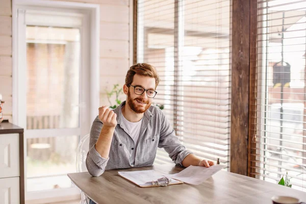 Jonge Europeaan die documenten leest terwijl hij thuis aan tafel zit — Stockfoto