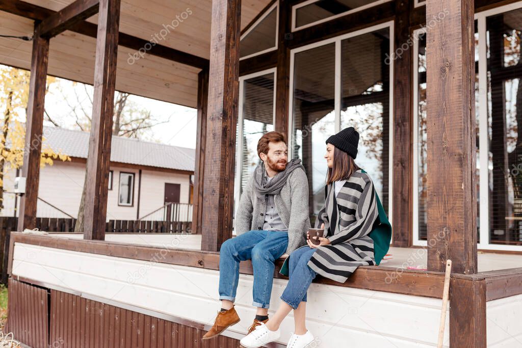 Happy young couple sitting outdoor, in front of their new home in autumn day