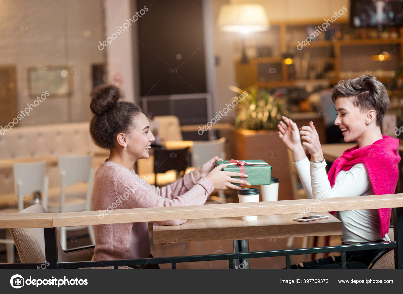 Happy woman congratulates her girlfriend with present box while sitting at cafe