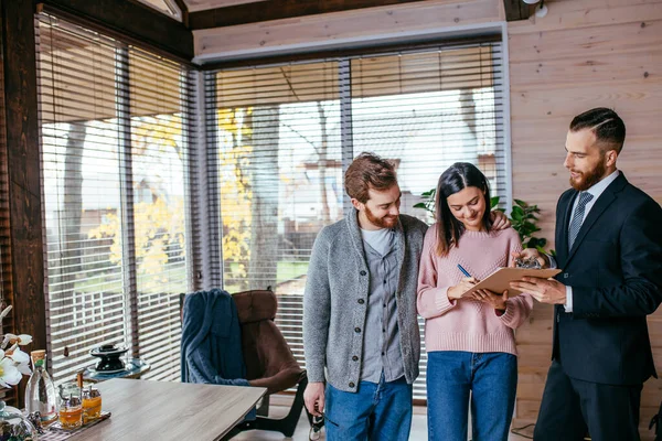 Pareja de clientes firmando papeles con corredor de hipotecas haciendo acuerdo de compra — Foto de Stock