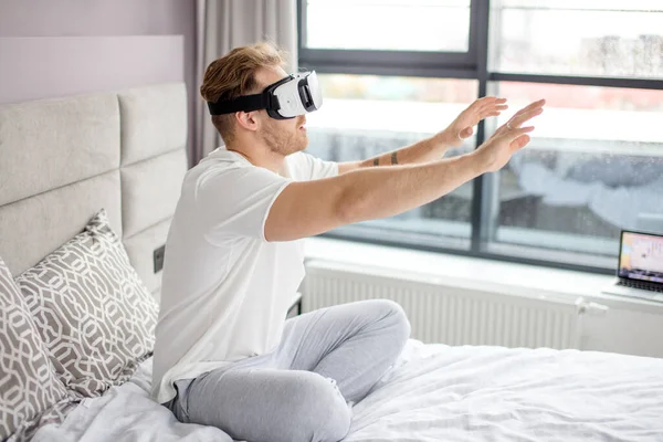 Chico está sentado en la cama y tratando de tocar la realidad virtual — Foto de Stock