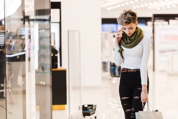 Vrouw met boodschappentassen, met behulp van een smartphone tijdens het winkelen in het winkelcentrum — Stockfoto