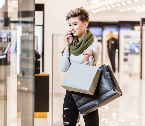 Vrouw met boodschappentassen, met behulp van een smartphone tijdens het winkelen in het winkelcentrum — Stockfoto