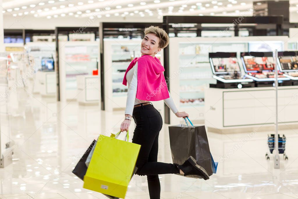 Smiling woman carrying some shopping bags with shops on the background