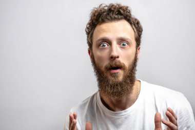 Kıvırcık saçlı ve sakallı beyaz adam kameraya şaşkın şaşkın bakıyor.