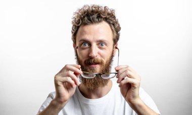 Kıvırcık saçlı ve sakallı beyaz adam kameraya şaşkın şaşkın bakıyor.