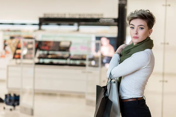 Leende kvinna som bär några shoppingväskor med butiker på bakgrunden — Stockfoto