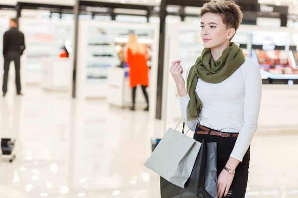 Glimlachende vrouw draagt een aantal boodschappentassen met winkels op de achtergrond — Stockfoto