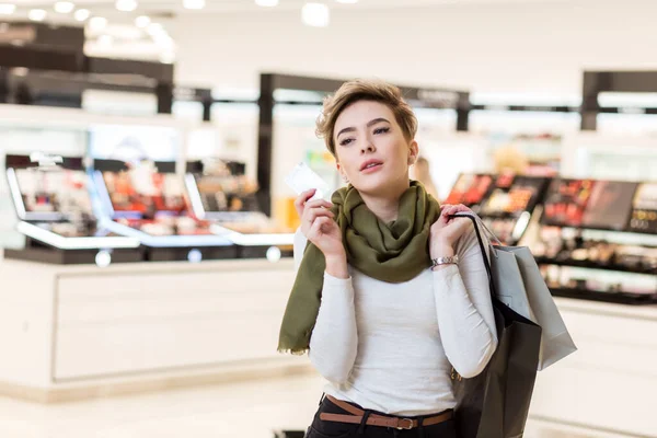Mujer rubia con bolsas de compras en una mano y tarjeta de crédito en otra en el centro comercial —  Fotos de Stock