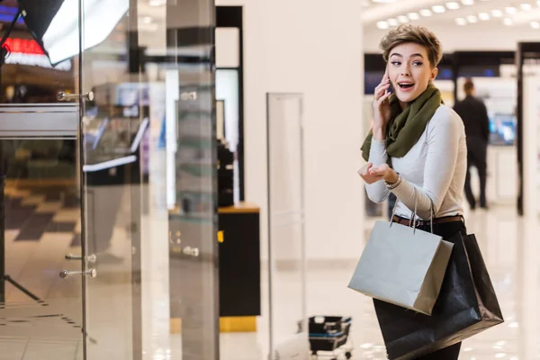 Vrouw met boodschappentassen, met behulp van een smartphone tijdens het winkelen in het winkelcentrum — Stockfoto