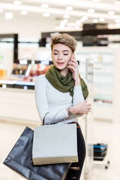 Vrouw met boodschappentassen, met behulp van een smartphone tijdens het winkelen in het winkelcentrum — Stockfoto