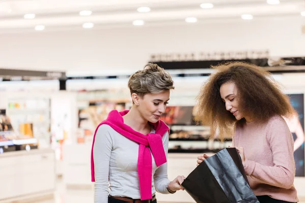 Brunette en blond kijken naar boodschappentas aan elkaar, bespreken aankopen. — Stockfoto