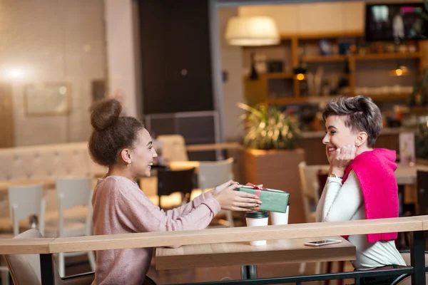 Счастливая женщина поздравляет свою подругу с подарочной коробкой, сидя в кафе. — стоковое фото