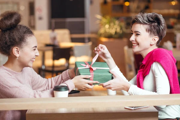 Счастливая женщина поздравляет свою подругу с подарочной коробкой, сидя в кафе. — стоковое фото