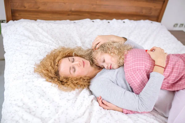 Retrato de madre e hija abrazándose mientras yacen en la cama — Foto de Stock