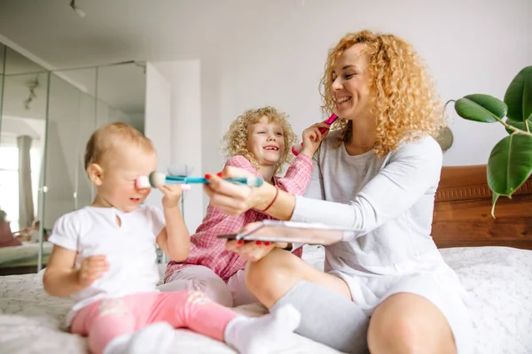 Genç aile ve çocuklar yatak odasında otururken fırçalarla eğleniyorlar. — Stok fotoğraf