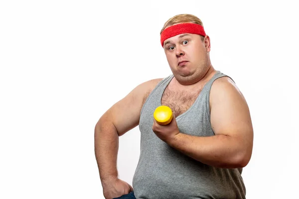 Gordo divertido hombre en rojo diadema muestra sus músculos con dummbell y emociones —  Fotos de Stock