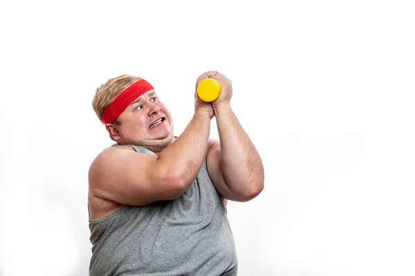 Grasso divertente uomo in fascia rossa mostra i muscoli con dummbell ed emozioni — Foto Stock