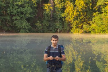 İyi görünümlü yürüyüşçü dağda dururken elinde bir cep telefonu tutuyor.