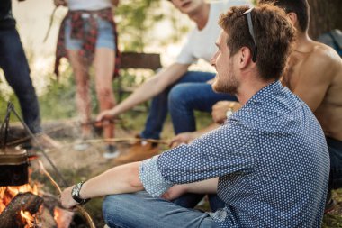 Boncuklu yakışıklı adam şenlik ateşinin yanında dinleniyor.