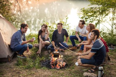 Genç çekici insanlar ellerinde sosislerle şenlik ateşinde çubuklar tutuyorlar.