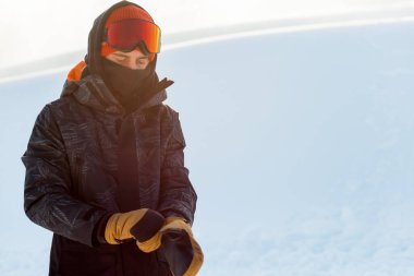 Genç snowboard sporcusu snowboard yapmadan önce eldivenlerini giyiyor.