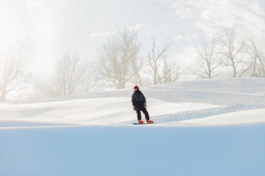Bir snowboardcu tahtada duruyor ve yana bakıyor.