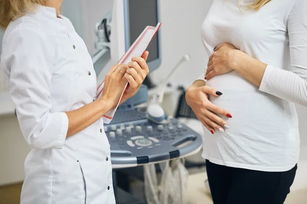 Gravid klient hålla hennes magsäck och prata med sjuksköterska — Stockfoto