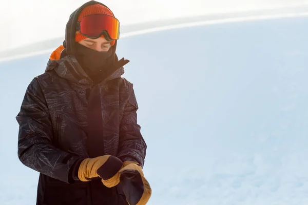 Молодий сноубордист у спортивному одязі одягає рукавички перед сноубордом — стокове фото