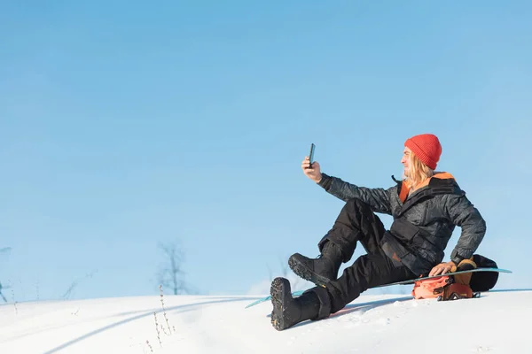 Alegre hombre rubio en invierno snowboard ropa sentado —  Fotos de Stock