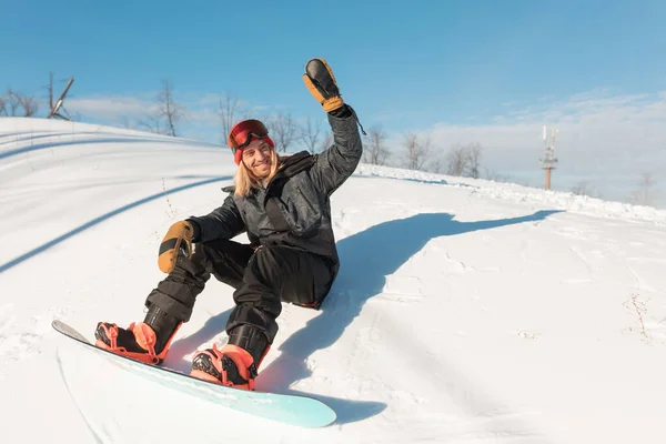 Cheerful sporty man is greeting somebody while sitting on the snowy peak — Stock Photo, Image