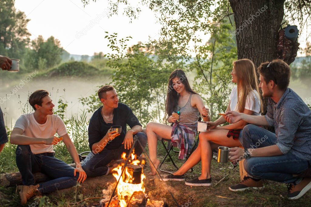 cheerful young people warming near the camp fire