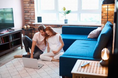 Çekici müstakbel aileler dizüstü bilgisayarlarıyla yerde otururlar.