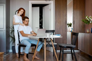 Kadın çalışan kocasına masaj yapıyor.